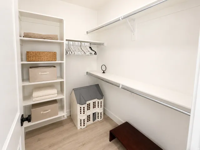Walk-in closet featuring built-in shelving, white walls, light wood-finish flooring, and multiple clothing rods