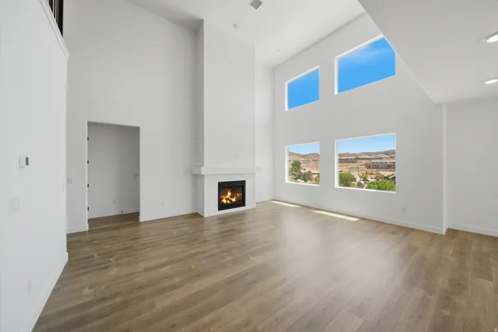 Spacious living area featuring a tall fireplace with a white shiplap-style surround and mantel, wood-finish flooring, and multiple windows providing ambient light and exterior views