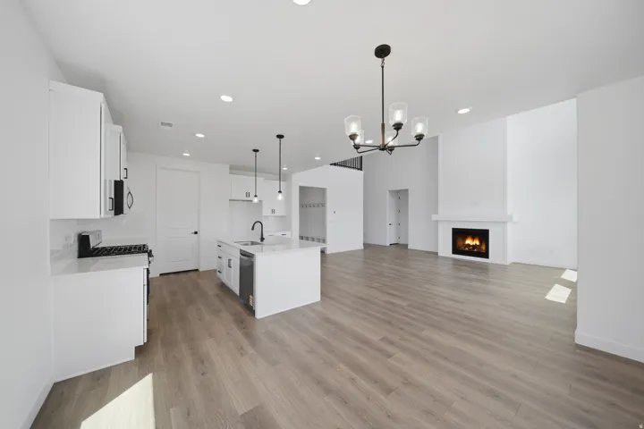 Bright kitchen and living area featuring wood-finish flooring, white cabinetry, a large kitchen island with integrated sink, and a modern fireplace with a white brick surround