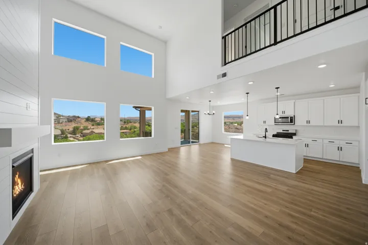Open-concept living area with wood-finish flooring, a contemporary fireplace with shiplap accent, and a kitchen featuring white cabinetry, an island, and stainless steel appliances