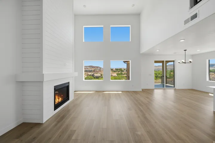 Two-story living area featuring a shiplap fireplace with mantel, light wood-finish flooring, and multiple windows
