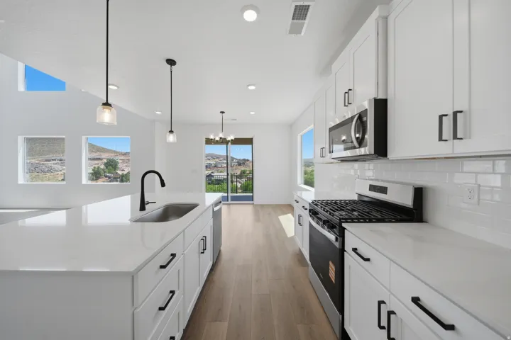 Open-concept kitchen featuring white cabinetry, light-toned countertops, stainless steel appliances, a white subway tile backsplash, and wood-finish flooring