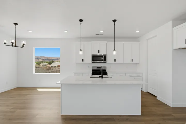 Open-concept living space featuring a kitchen island with pendant lighting, white cabinetry with black hardware, wood-finish flooring, and a large window with distant mountain scenery