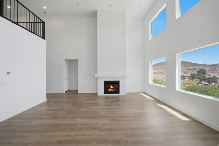 Two-story living area with wood-finish flooring, a contemporary fireplace with shiplap-style surround, and multiple windows displaying a distant mountainous landscape