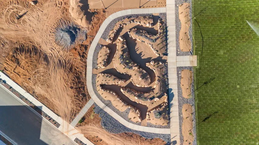 Aerial perspective showcasing a designed landscape feature with a meandering pathway, surrounding dry-stacked stone beds, and a manicured lawn area