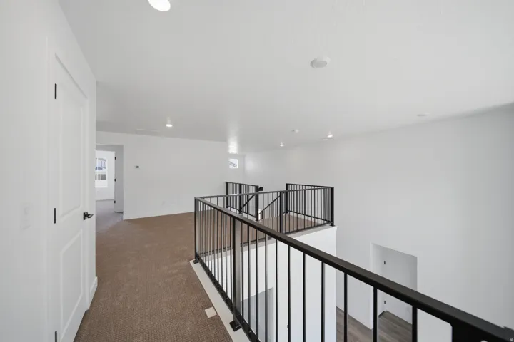Spacious upper-level landing featuring neutral carpeting, recessed lighting, and a modern black metal railing overlooking the floor below