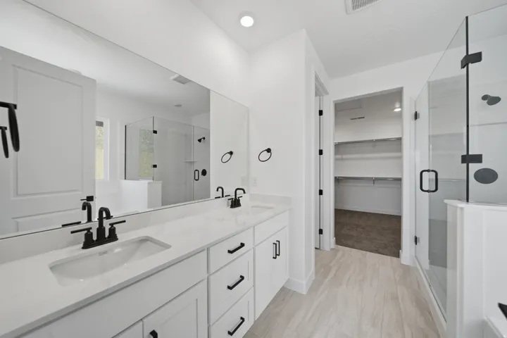 Contemporary bathroom featuring a double vanity with stone countertops and matte black fixtures, a spacious glass-enclosed shower, and wood-finish flooring