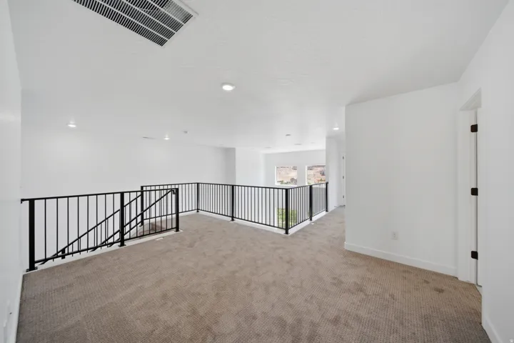 Upper-level landing featuring carpet flooring, crisp white walls, recessed lighting, and a contemporary black metal railing system
