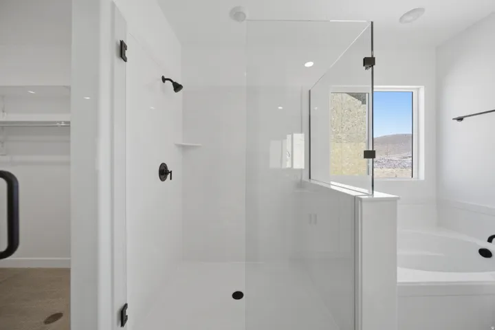 Modern bathroom featuring a glass-enclosed shower with matte black fixtures, a built-in tub, and a window with mountain scenery
