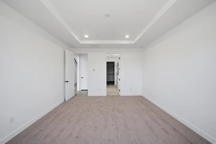 Spacious room featuring a tray ceiling with recessed lighting, neutral carpeting, white baseboards, and painted interior doors with dark hardware