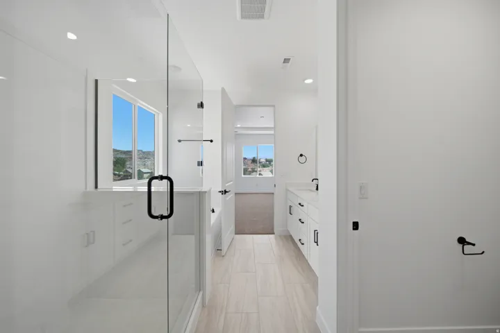 Spacious bathroom featuring a glass-enclosed shower, dual vanity with undermount sinks, white cabinetry, and large format tile flooring