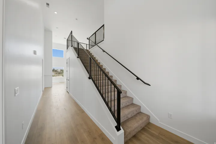 Open-concept entryway featuring wood-finish flooring, a carpeted staircase with black iron railings, and high ceilings