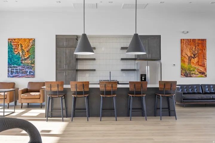 Spacious open-concept area featuring a kitchen island with seating for five, two contemporary pendant lights, wood-finish flooring, and built-in cabinetry with open shelving
