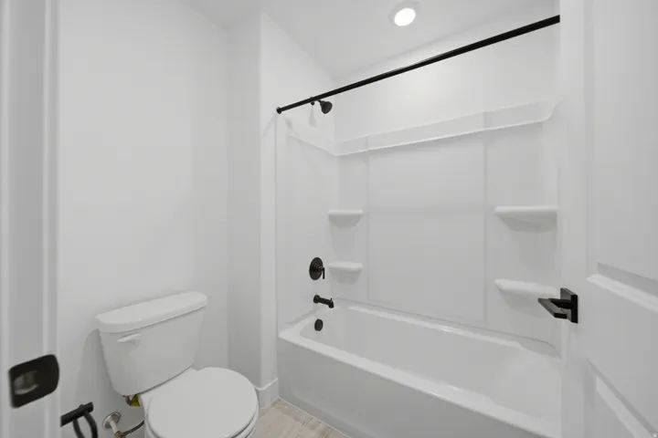 Full bathtub with a matte black shower fixture, white shower surround, and black shower curtain rod