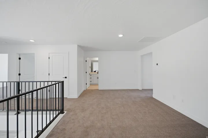 Carpeted upper level featuring a black metal railing, white doors with black hardware, recessed lighting, and a visible bathroom vanity beyond
