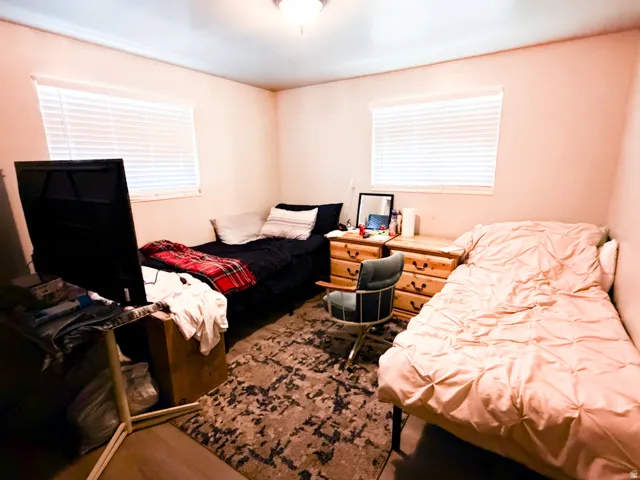 Room featuring wood-finish flooring, two windows with horizontal blinds, and a textured area rug