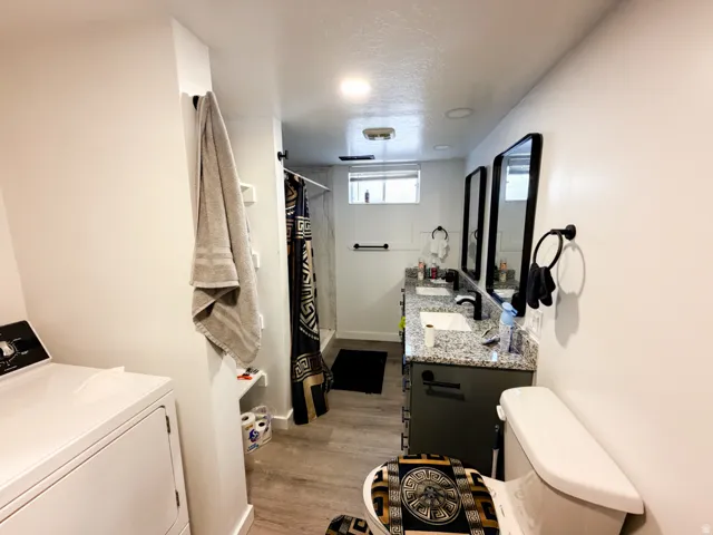 Bathroom featuring a dual vanity with granite countertops, wood-finish flooring, a shower with a dark-patterned curtain, and a window providing natural light