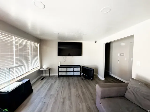 Spacious living area featuring wood-finish flooring, recessed ceiling lighting, and a wide window with horizontal blinds