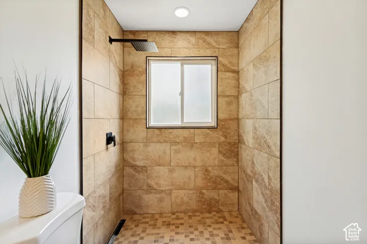 Jack and Jill Bathroom connected to primary bedroom. Walk-in shower featuring large format wall tiling, mosaic floor tiling, a frosted window, and matte black fixtures