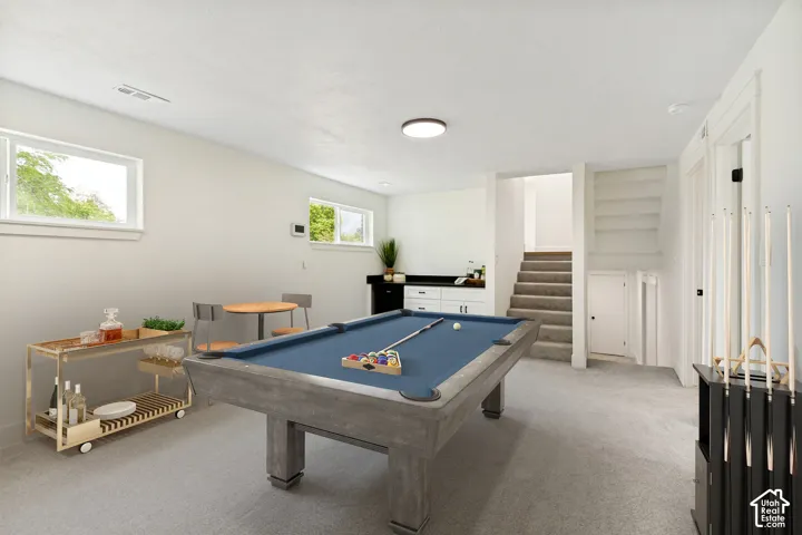 Finished basement featuring light gray carpet flooring, white walls, two windows, and a built-in wet bar with white cabinetry and a dark countertop