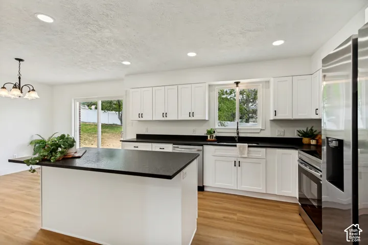 Modern kitchen featuring a central island with a dark countertop, white cabinetry with dark hardware, stainless steel appliances, and LVP flooring