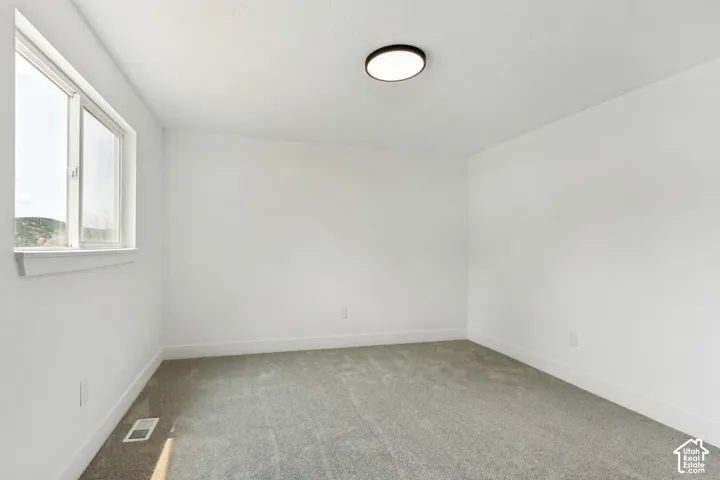 Primary bedroom featuring a double-pane window, flush-mount ceiling light, white walls, white baseboards, and gray carpeting