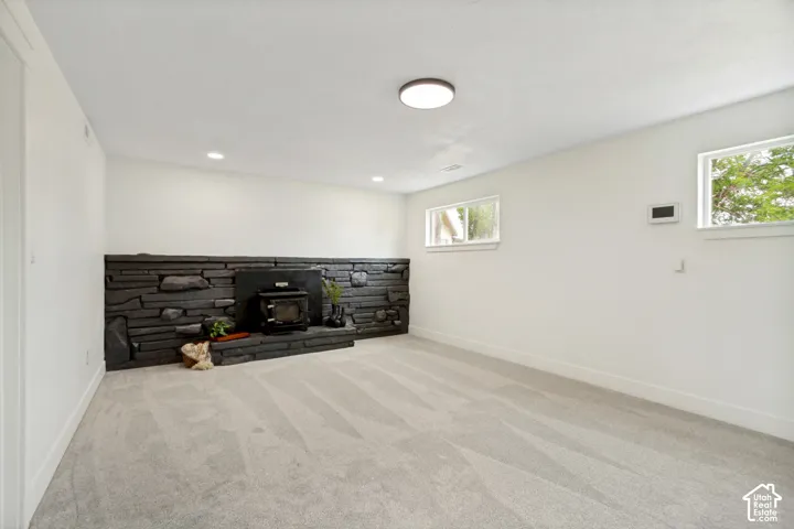 Spacious flex/family room featuring a dark stacked stone accent wall with a wood-burning stove, light gray carpeting, and white baseboards. This room has the dry bar.