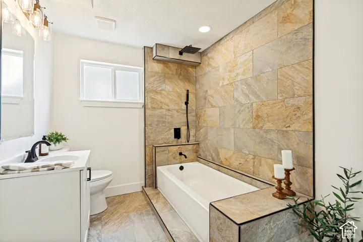 Bathroom featuring a tiled accent wall, white soaking tub with matte black fixtures, a rain shower head, and a white vanity with a rectangular undermount sink