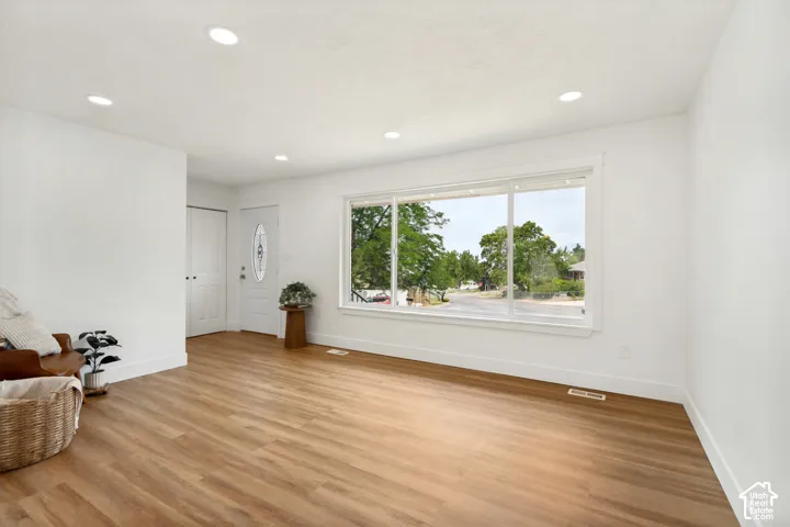 Bright interior space featuring a large picture window, LVP flooring, recessed lighting, white baseboards, and a white entry door with an oval glass insert