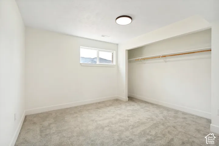 Neutral-toned large 4th bedroom featuring a window with a mountain backdrop, plush grey carpeting, and an open closet with a single hanging rod