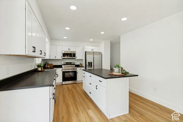 Kitchen featuring white cabinetry with black hardware, dark countertops, LVP flooring, recessed lighting, and stainless steel appliances