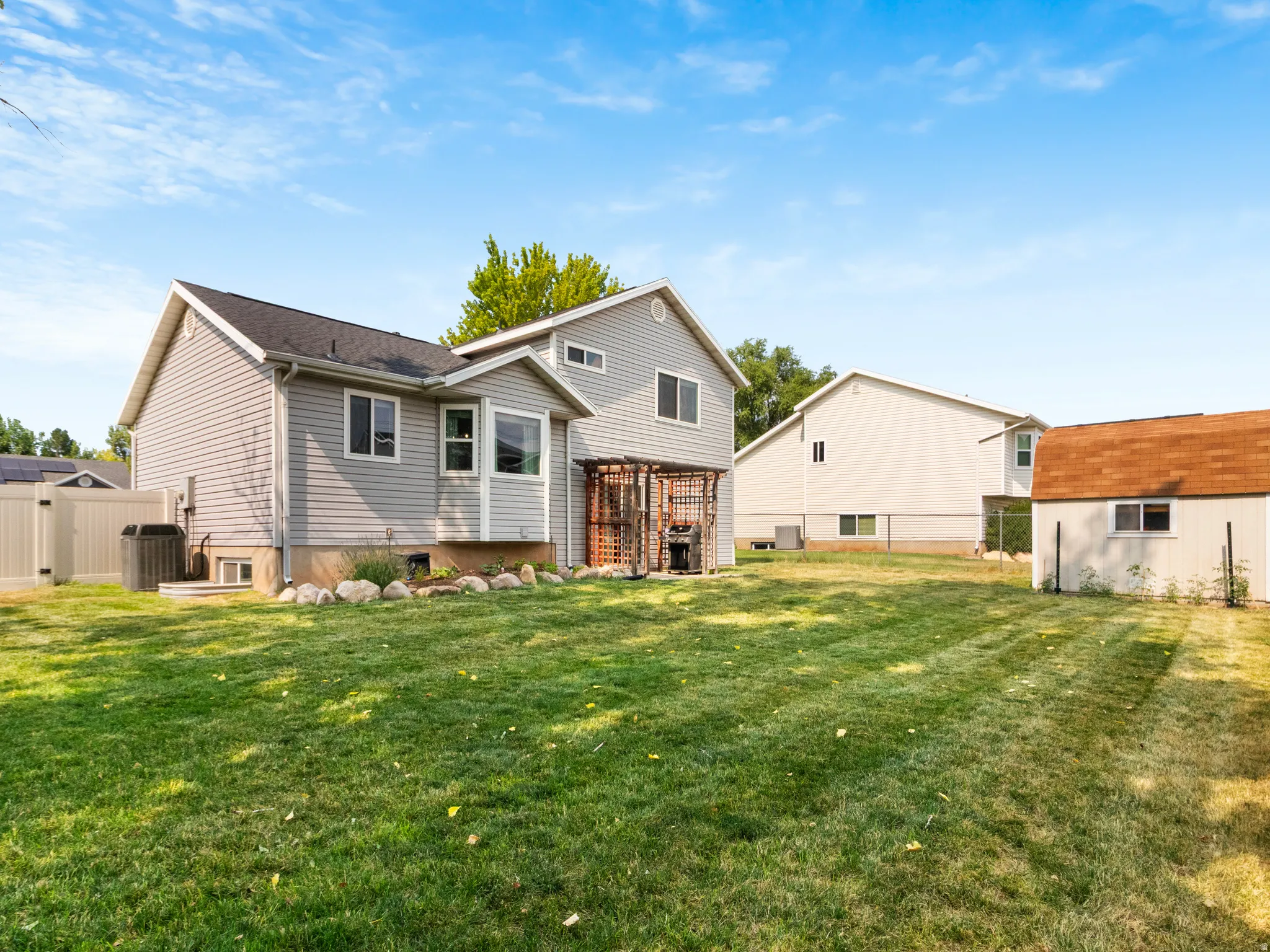 Spacious backyard featuring a lush lawn, vinyl privacy fencing, and a detached storage shed with a shingled roof