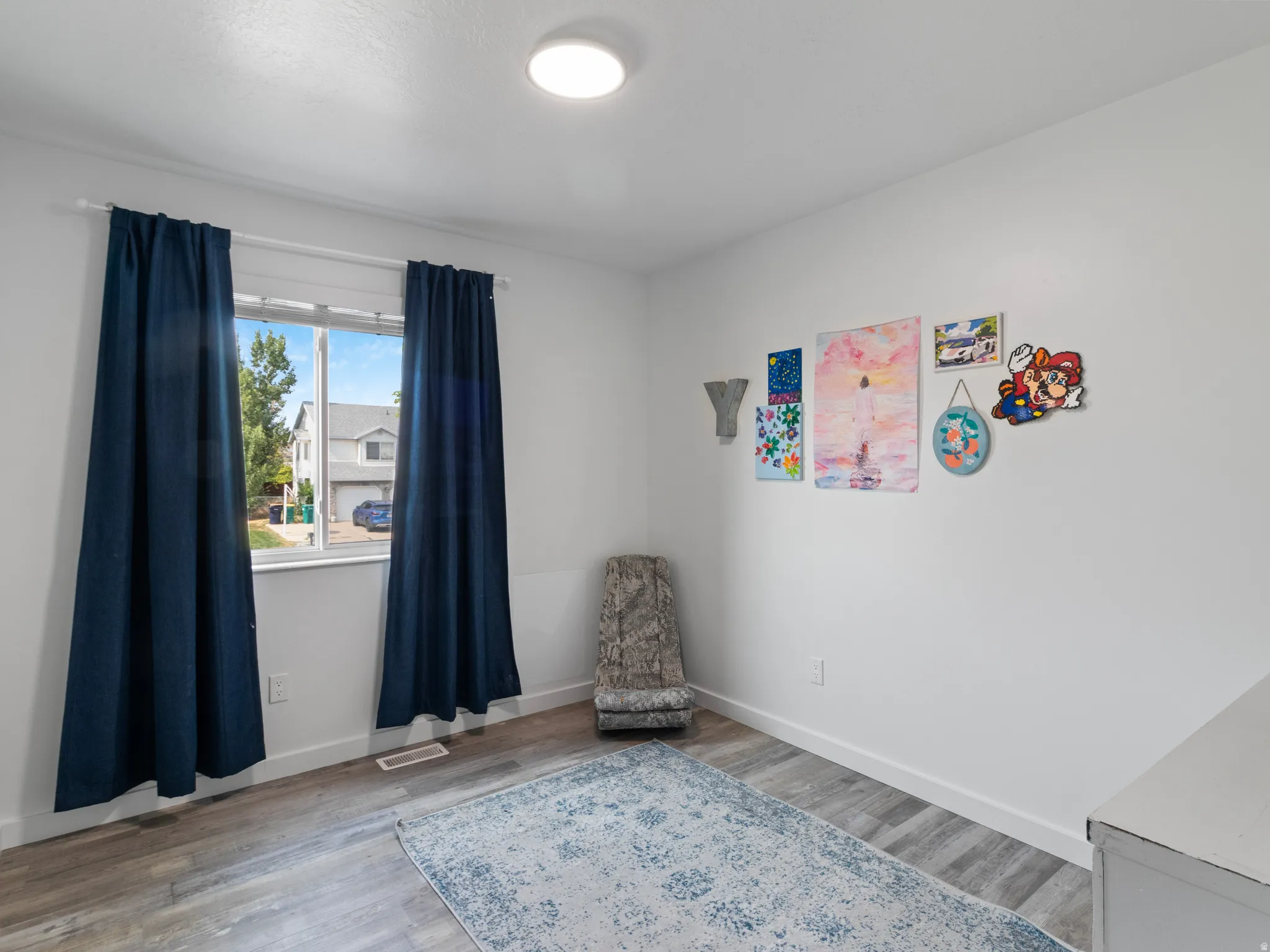 Bright interior space featuring a window with natural light, wood-finish flooring, white baseboards, and a flush-mount ceiling light