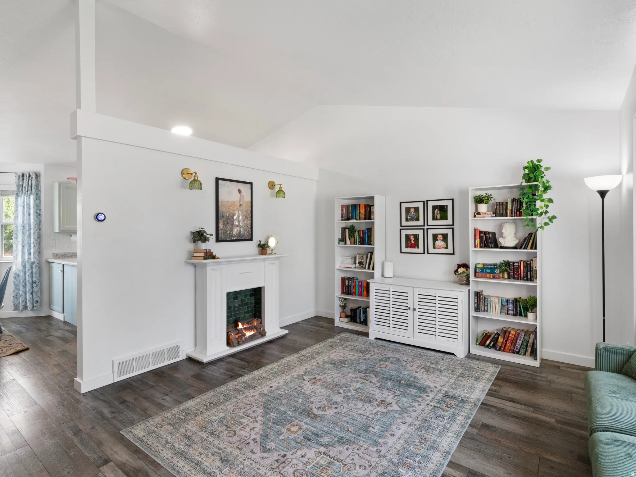 Vaulted ceiling living space with a decorative fireplace, wood-finish flooring, white walls, and shelving