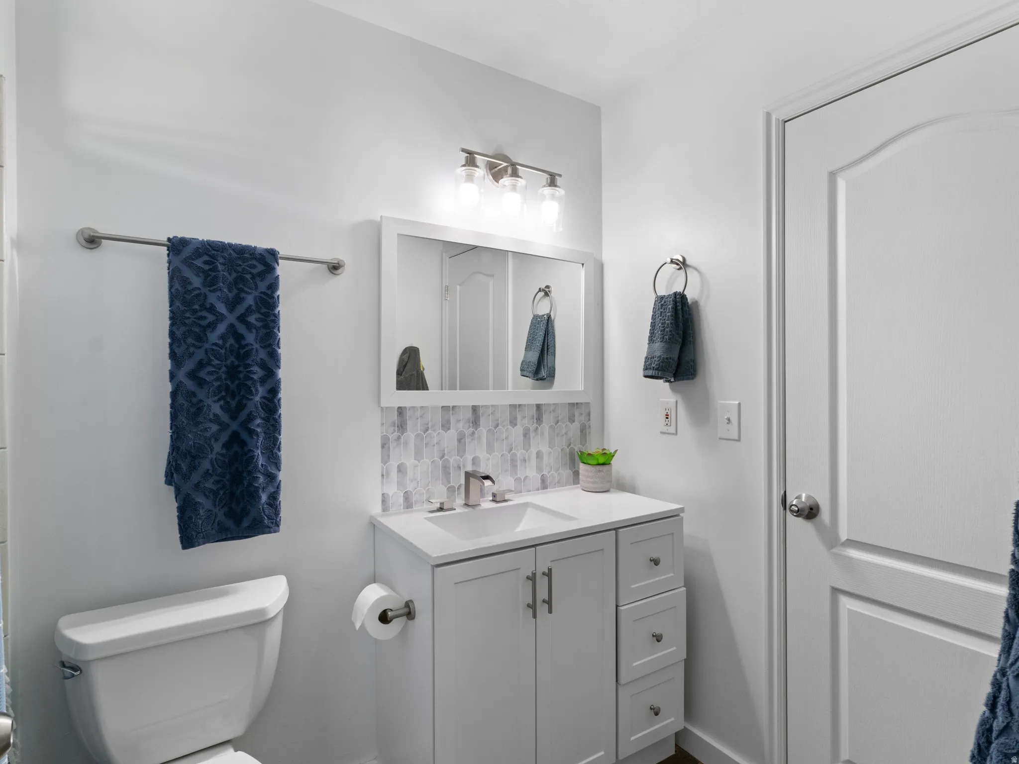 Bathroom featuring a white vanity with integrated sink, a tiled backsplash, and a modern light fixture