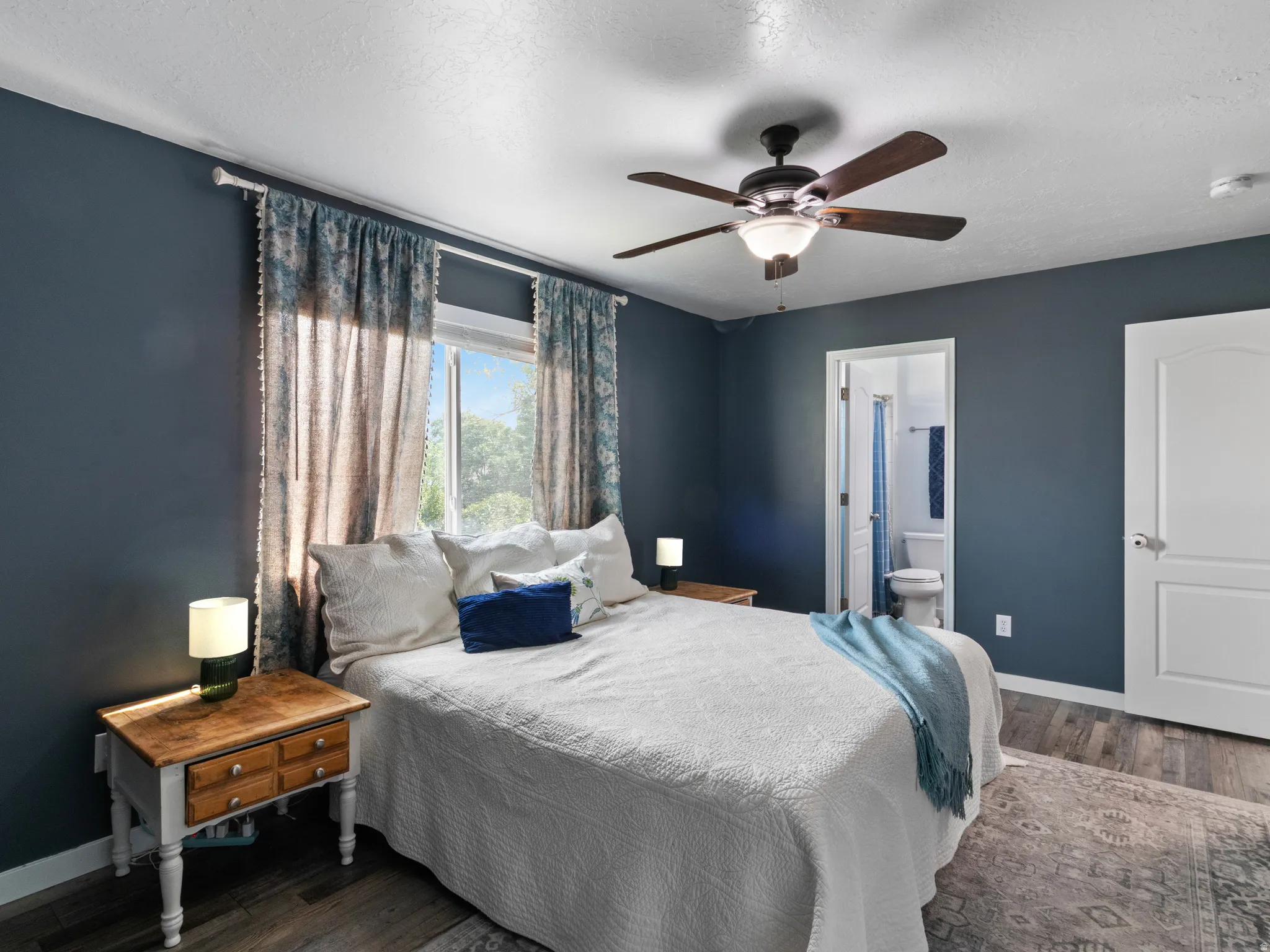 Spacious room featuring dark blue walls, wood-finish flooring, and a ceiling fan with integrated lighting