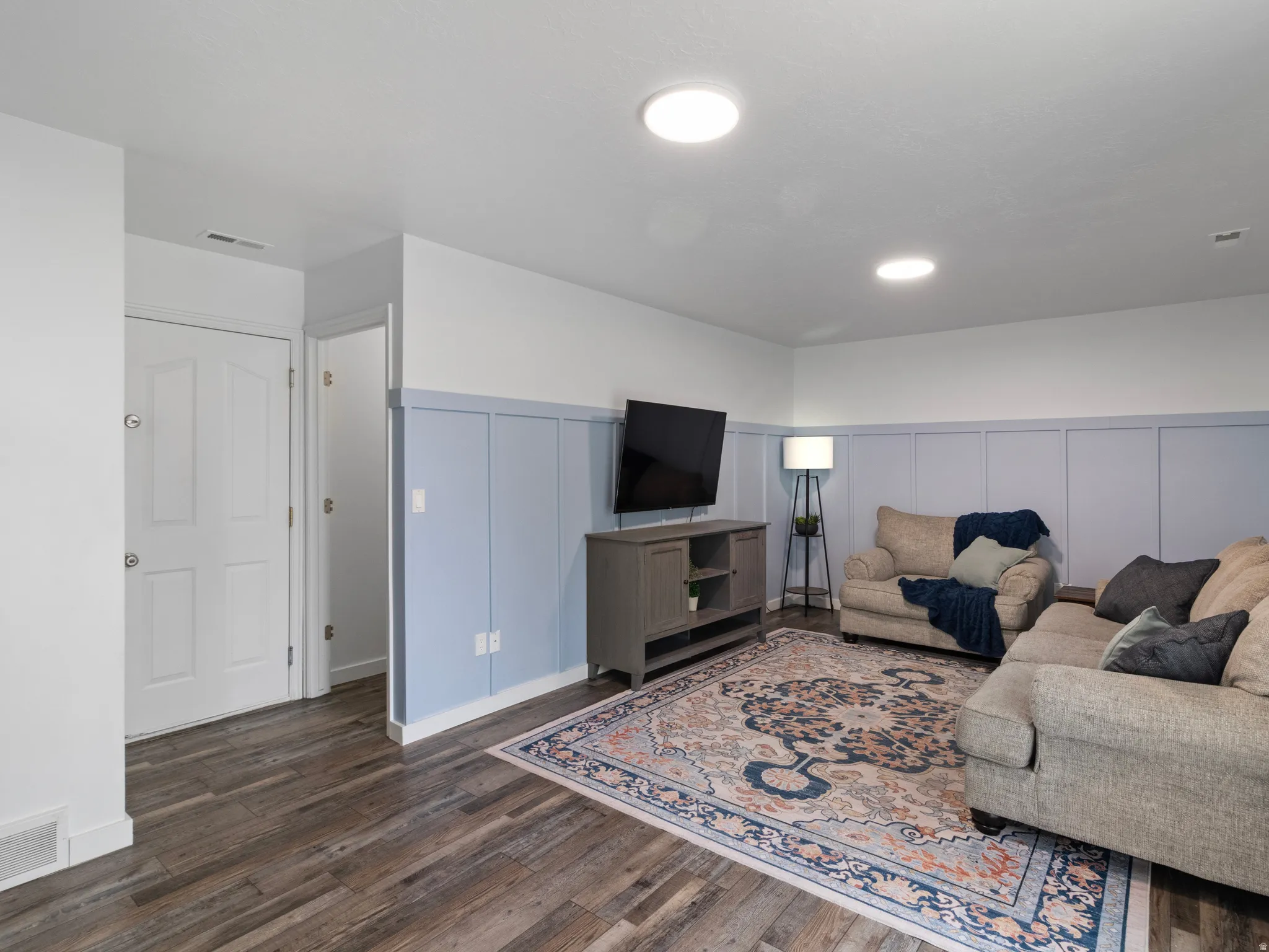Wood-finish flooring throughout, complemented by a light blue wainscoting accent wall and recessed ceiling lighting