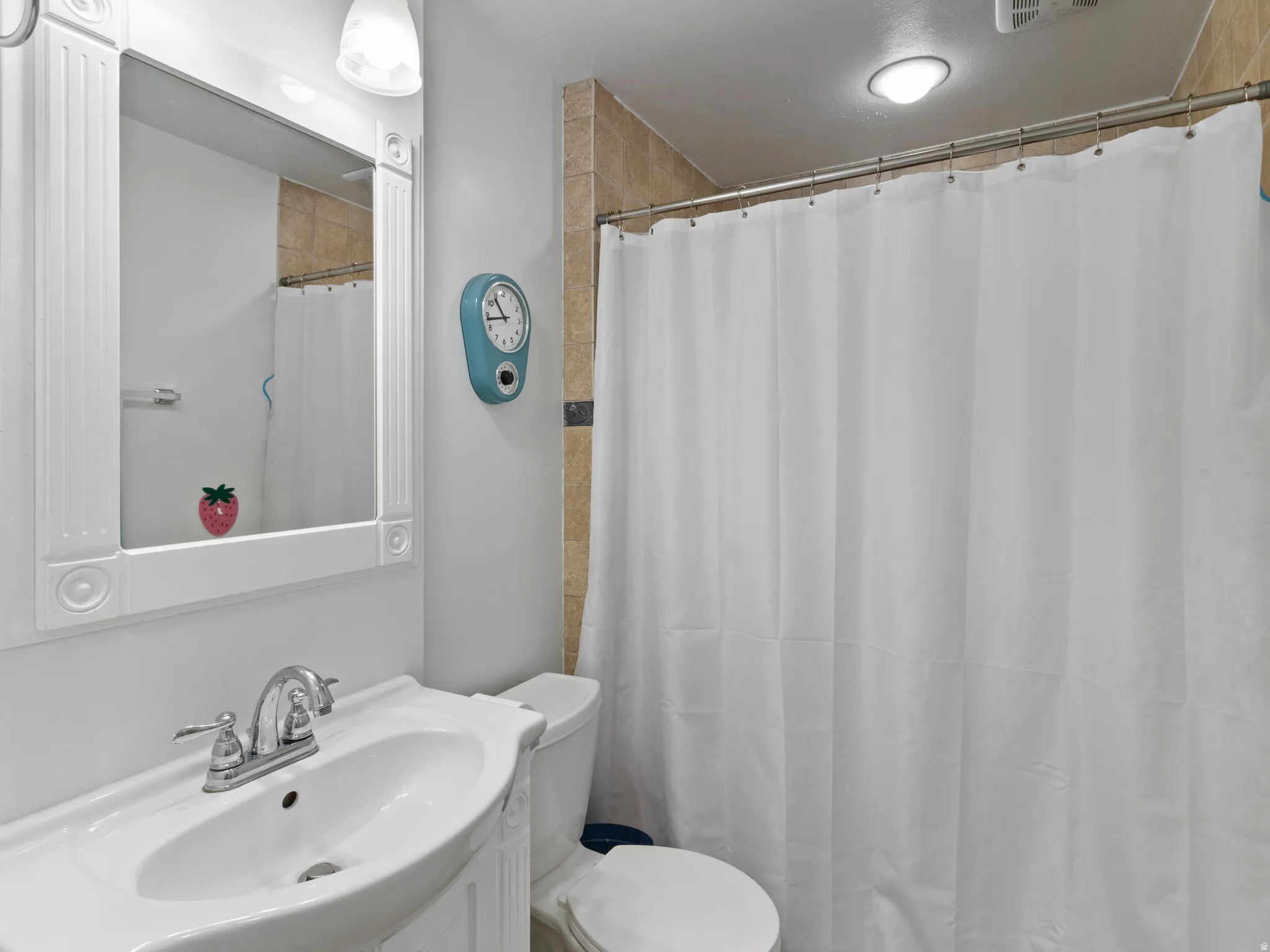 Bathroom featuring a shower with tiled surround, white vanity sink with chrome fixtures, coordinating white toilet, and a framed mirror