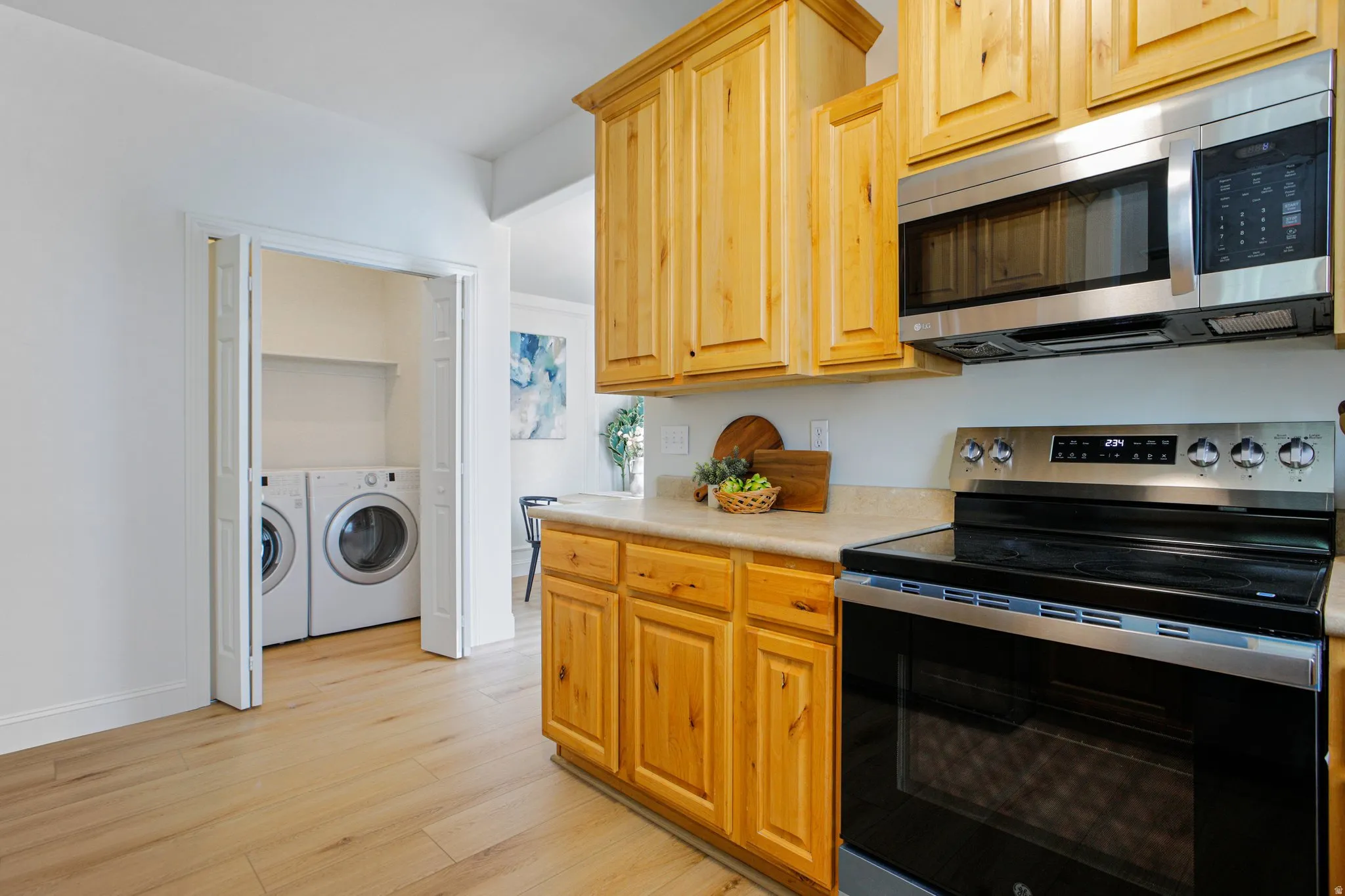 Kitchen featuring natural wood cabinetry, light-toned countertops, and stainless steel appliances including a range and over-the-range microwave