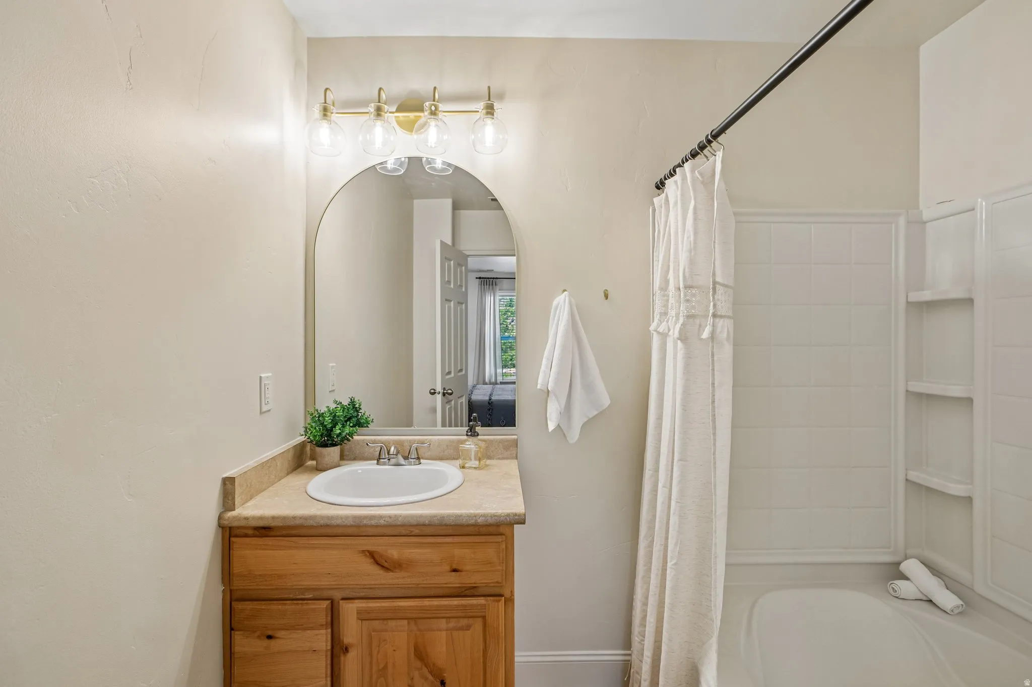 Bathroom featuring a wood-finish vanity with a light-colored countertop and an arched mirror
