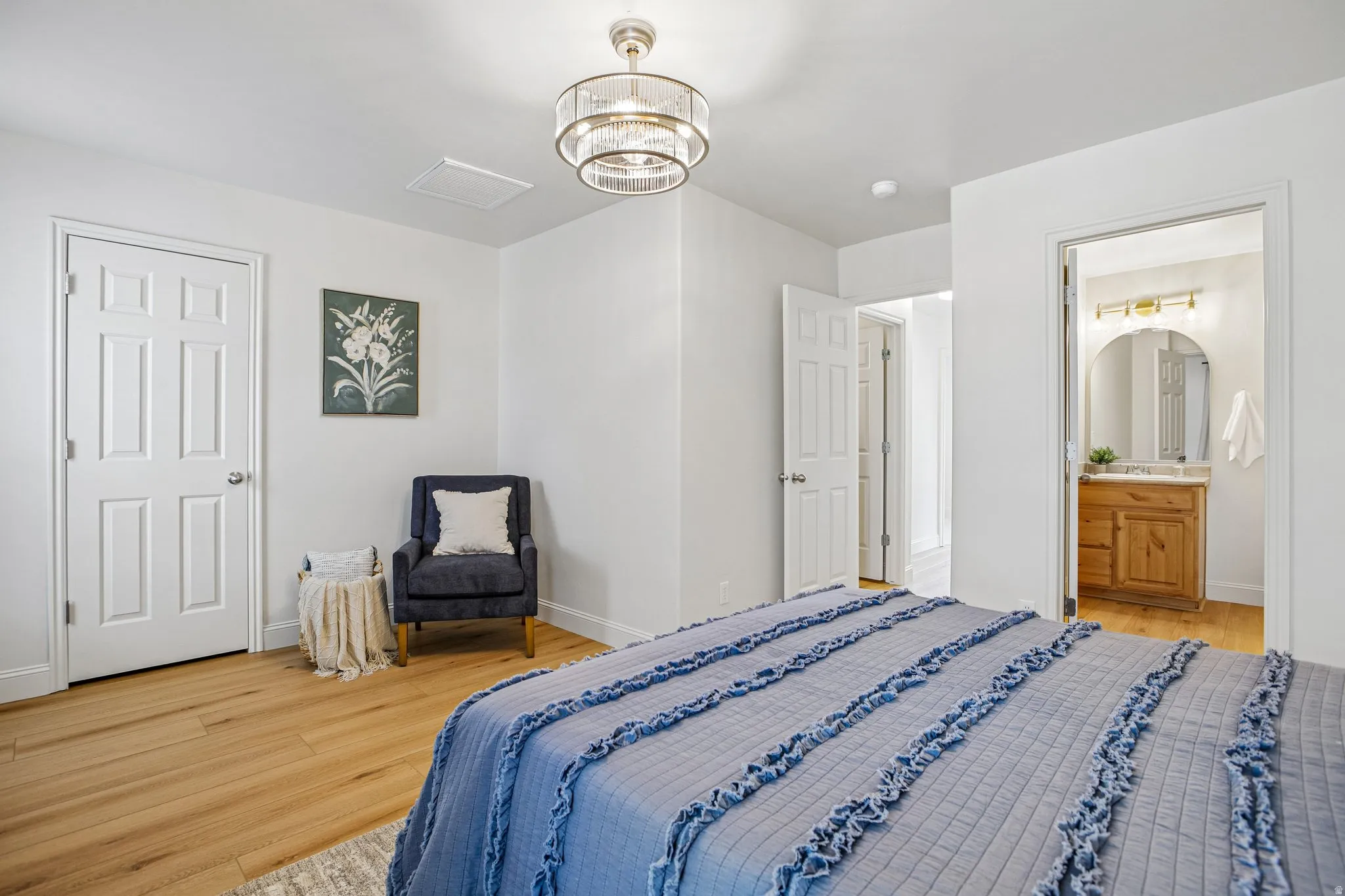 Light wood-finish flooring complements the bright white walls of this bedroom, featuring a contemporary semi-flush mount ceiling light