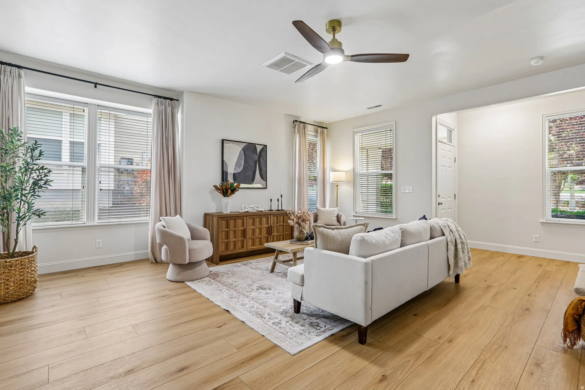 Spacious living area featuring light wood-finish flooring and ample natural light from multiple windows
