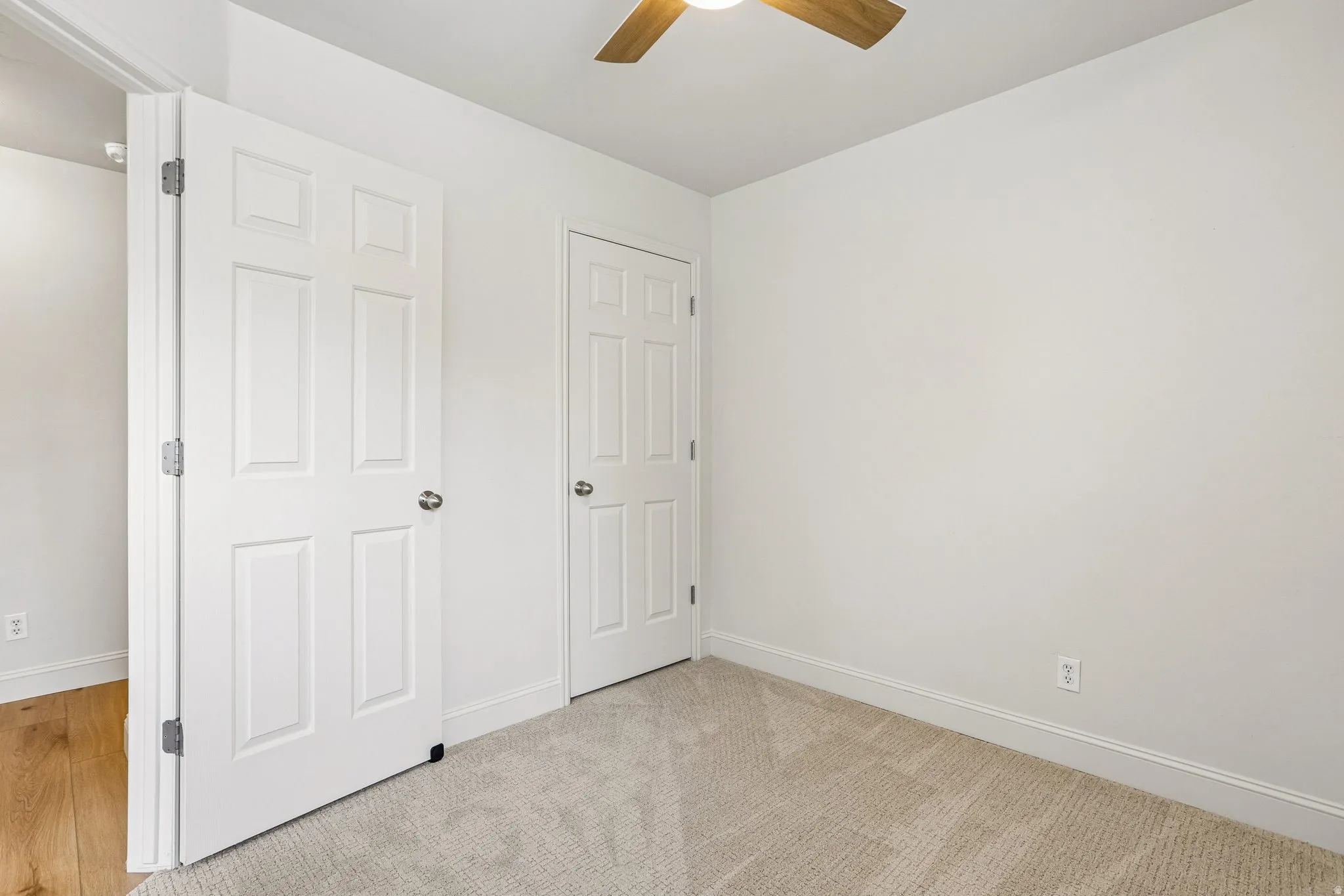 Room featuring light beige carpeting, white walls, and a ceiling fan with wood-finish blades