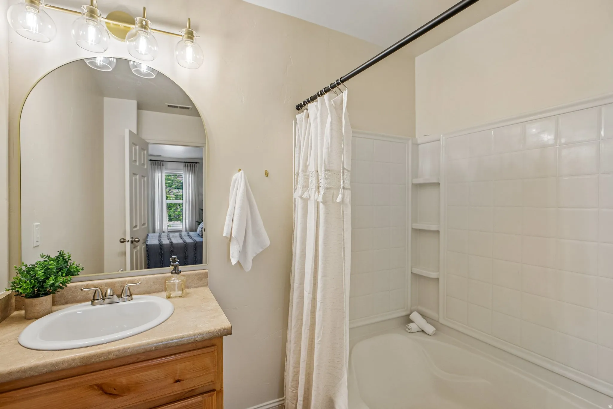 Bathroom featuring a wood-finish vanity with an oval sink, an arched mirror, and a brass-finish vanity light fixture