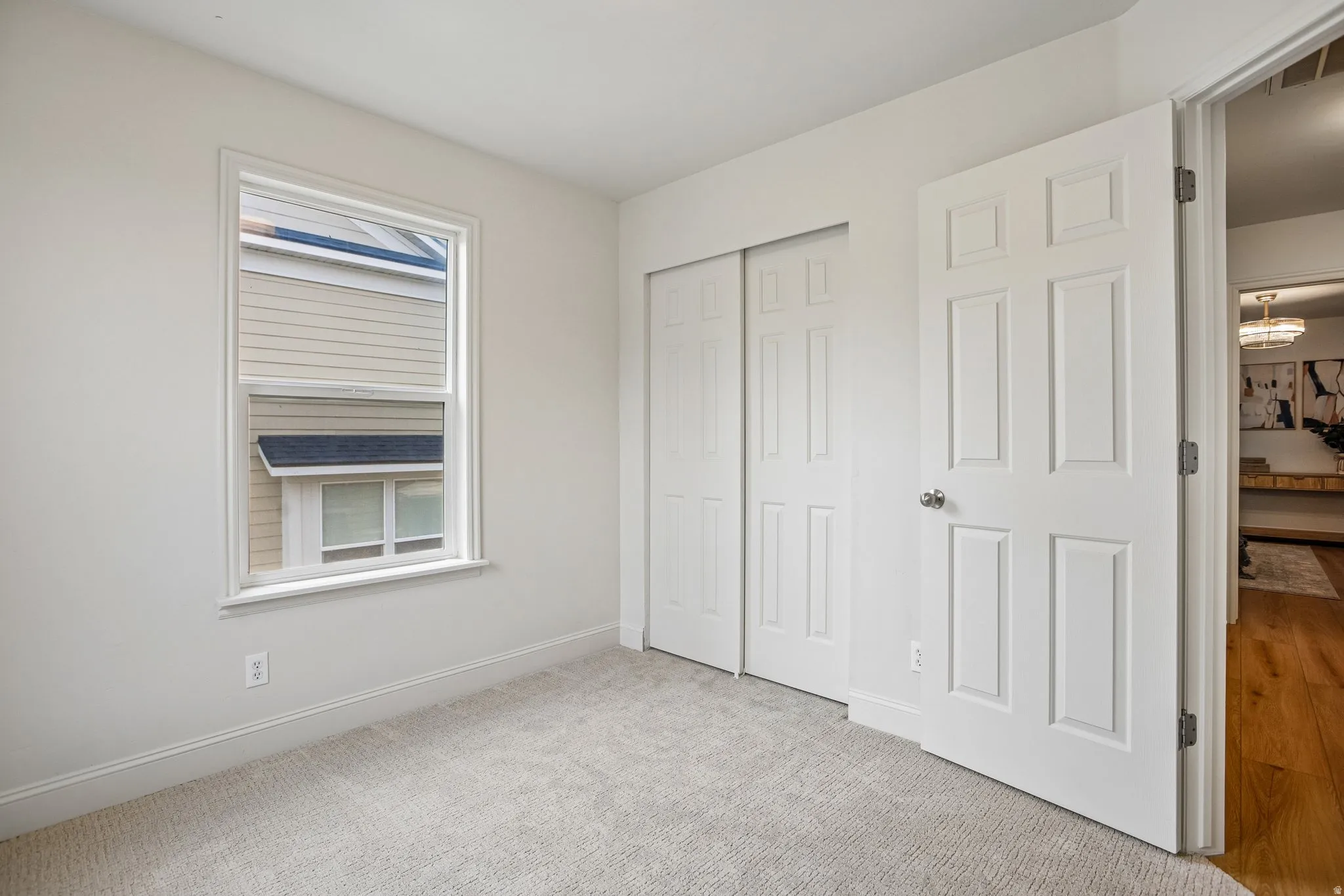 Bright room featuring a window with white trim, light-colored carpeting, white baseboards, and a bi-fold closet with panel doors