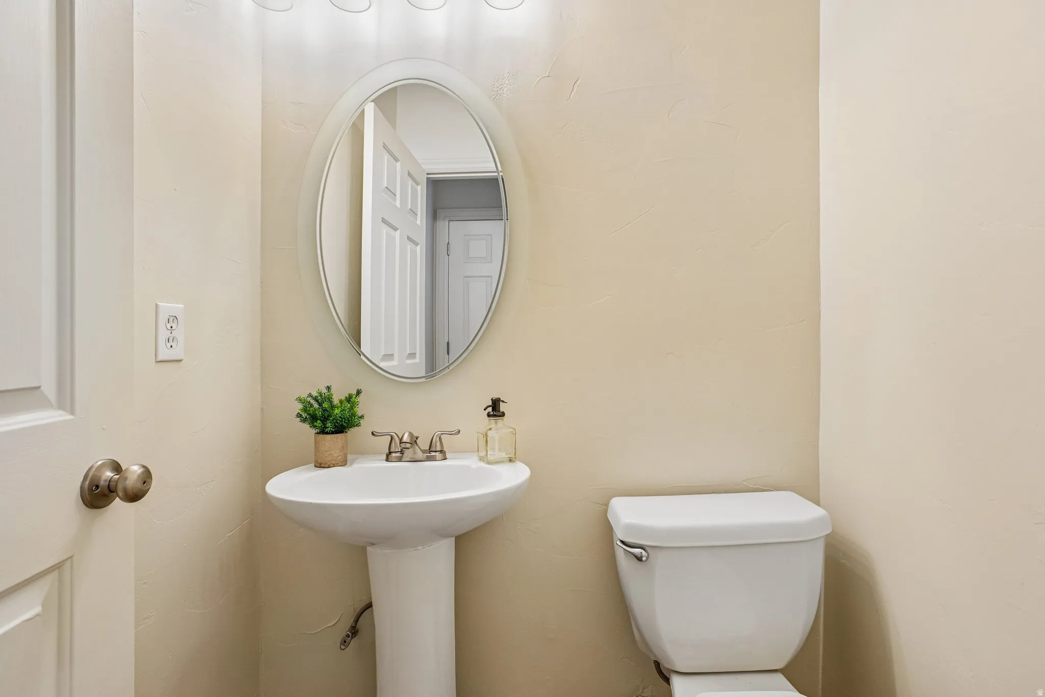 Bathroom featuring a white pedestal sink, an oval mirror, and a toilet