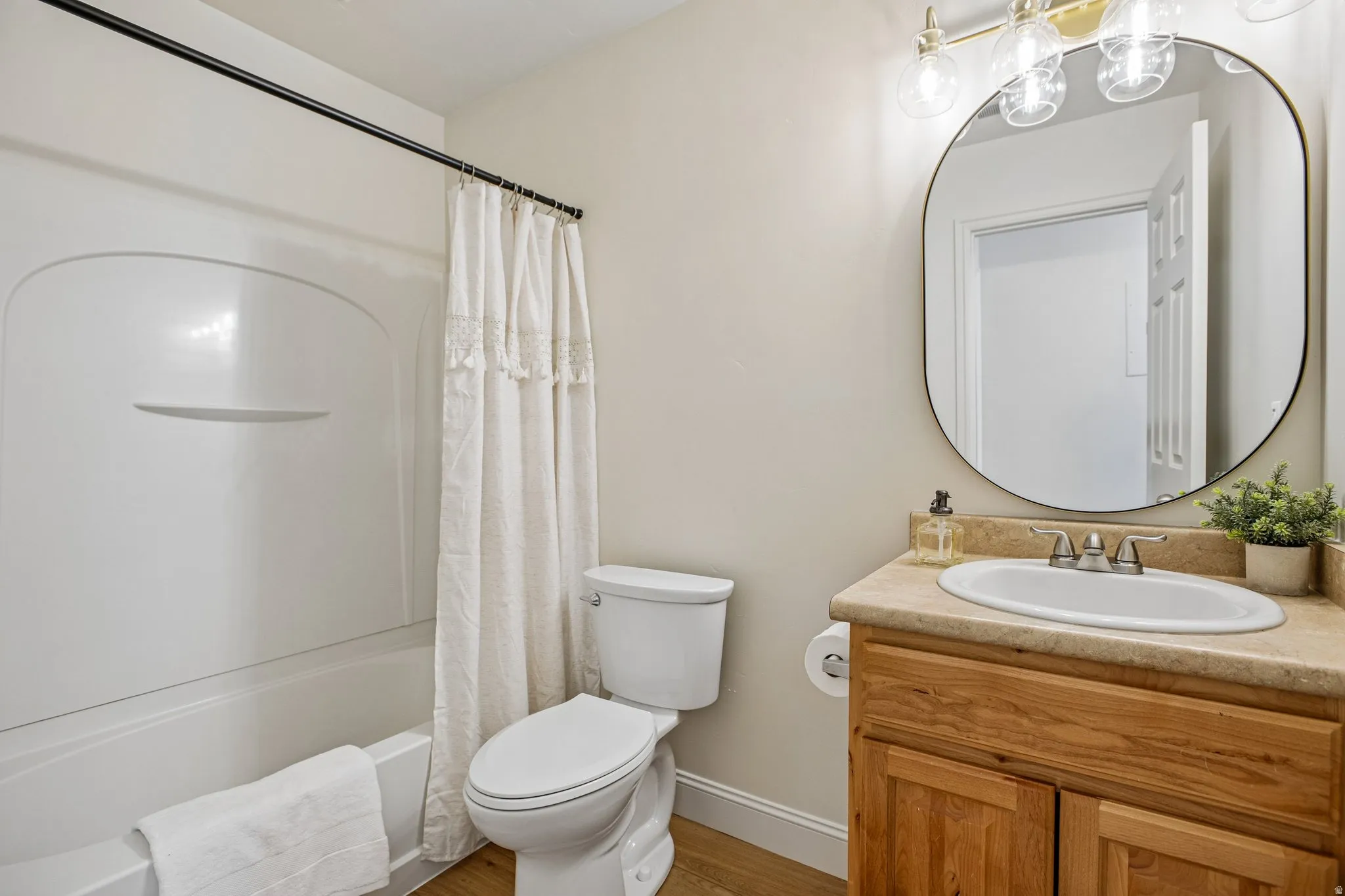 Bathroom featuring a white tub/shower combination, a toilet, a wood-finish vanity with a built-in sink, and a framed oval mirror