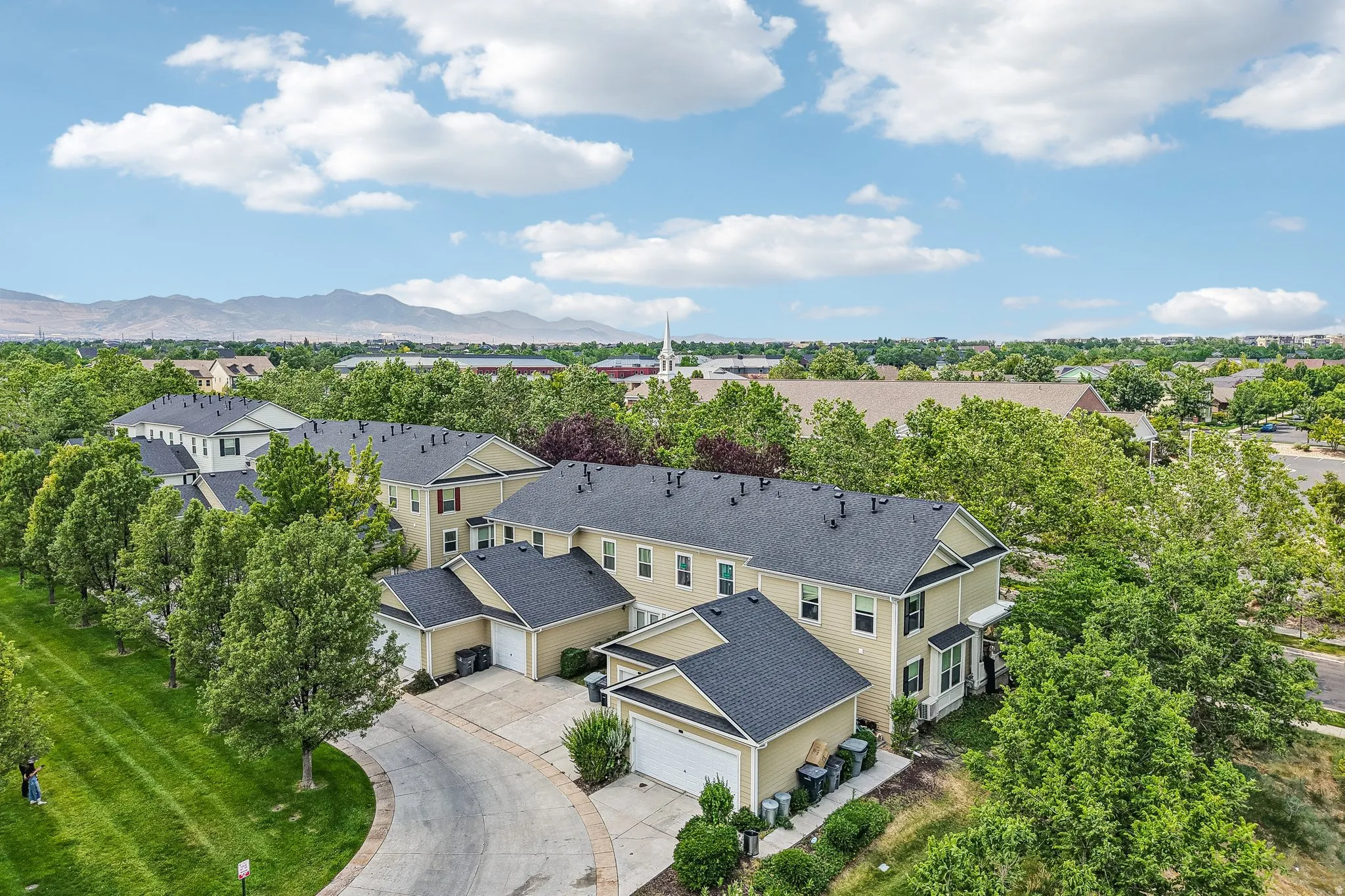 Aerial perspective showcasing a community of townhome-style residences with tan siding, dark shingle roofs, and attached garages