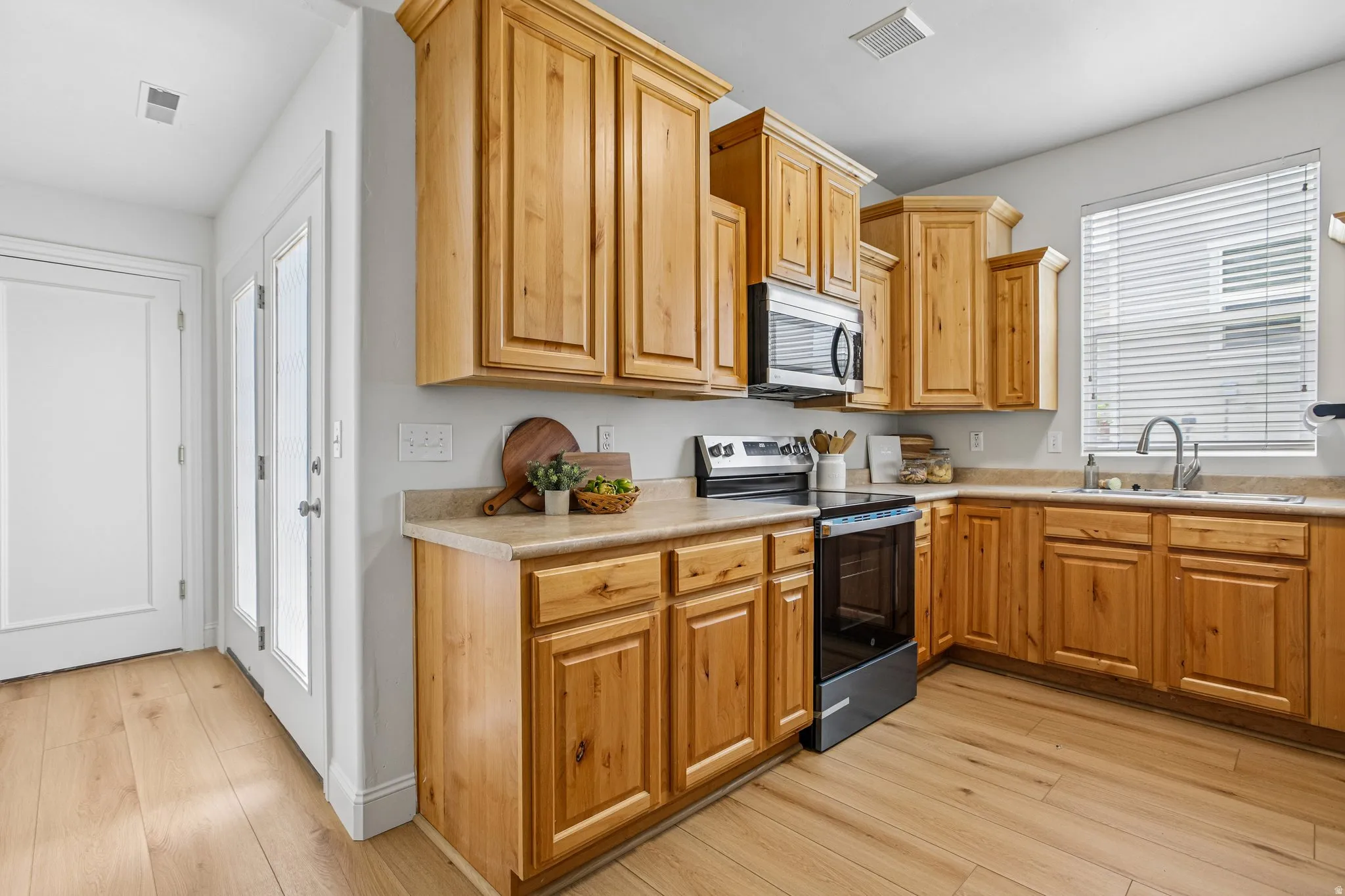 Kitchen featuring wood-finish cabinetry, light-toned countertops, stainless steel appliances, a window with horizontal blinds, and wood-finish flooring