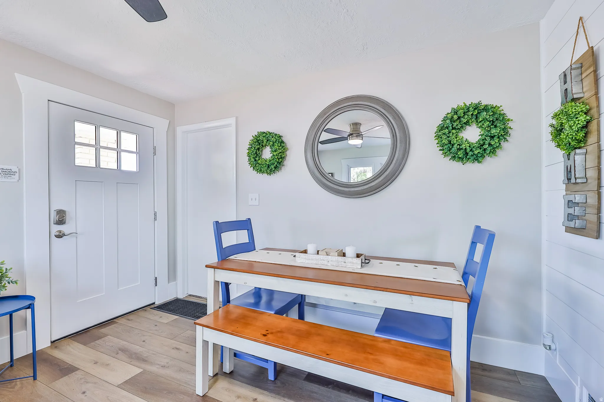 Dining area featuring wood-finish flooring, a white paneled entry door with clear glass lites, a ceiling fan, and a shiplap accent wall